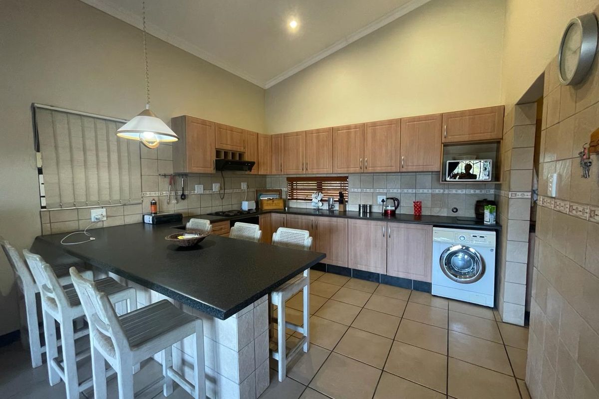 Spacious kitchen featuring wood-finish cabinetry, dark countertops, a central island with breakfast bar seating, and integrated laundry appliances.