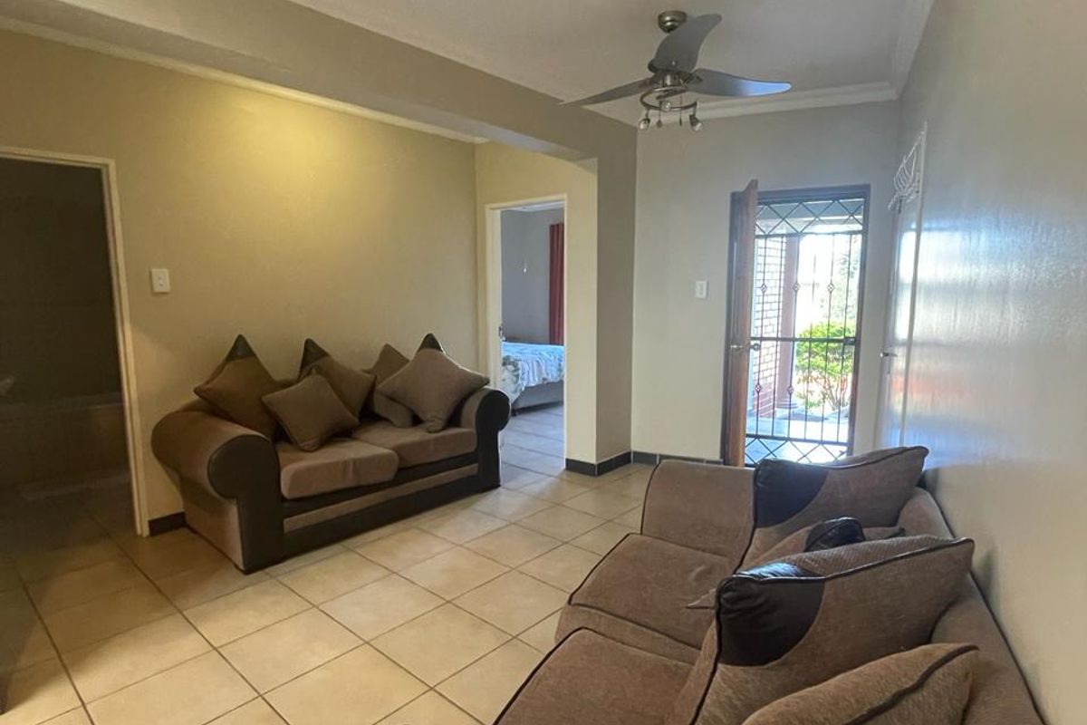 A living room featuring tiled flooring, a ceiling fan, and a security gate leading to the exterior.