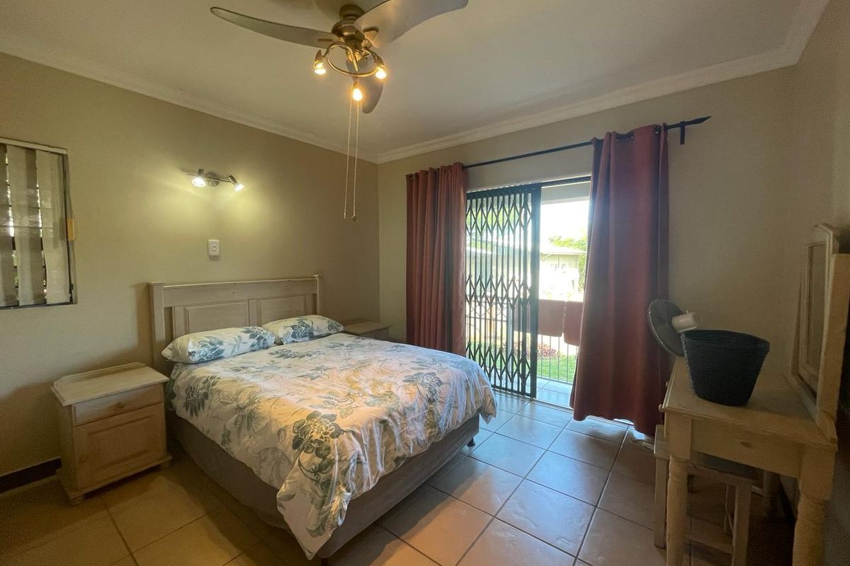 A bedroom featuring tiled flooring, a ceiling fan, and a sliding glass door with a security gate providing access to the exterior.
