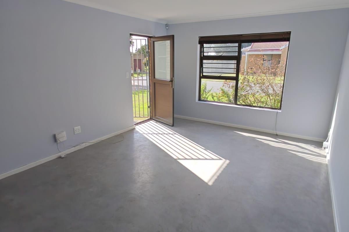A bright, empty living room featuring polished concrete flooring, a security gate at the entrance, and large windows providing natural light.