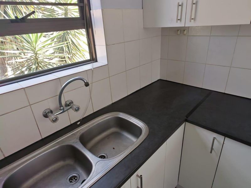 A functional kitchen area featuring white cabinetry, dark laminate countertops, a double bowl stainless steel sink, and tiled splashbacks.