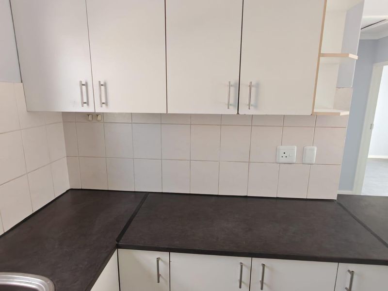 A functional kitchen area featuring white cabinetry, dark laminate countertops, a stainless steel sink, and a neutral tiled backsplash.