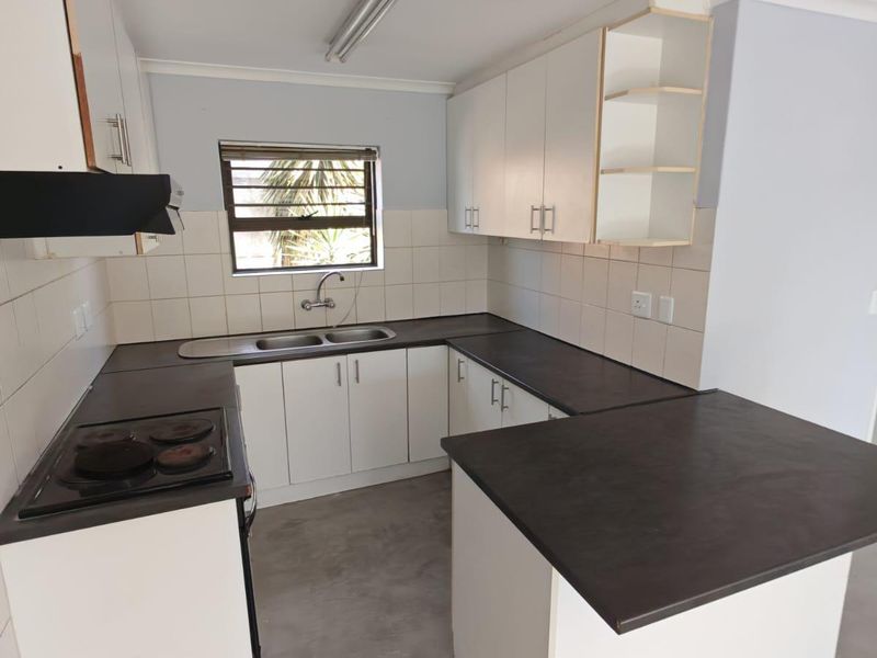 A functional, empty kitchen featuring white cabinetry, dark laminate countertops, a built-in electric hob, and a tiled backsplash.