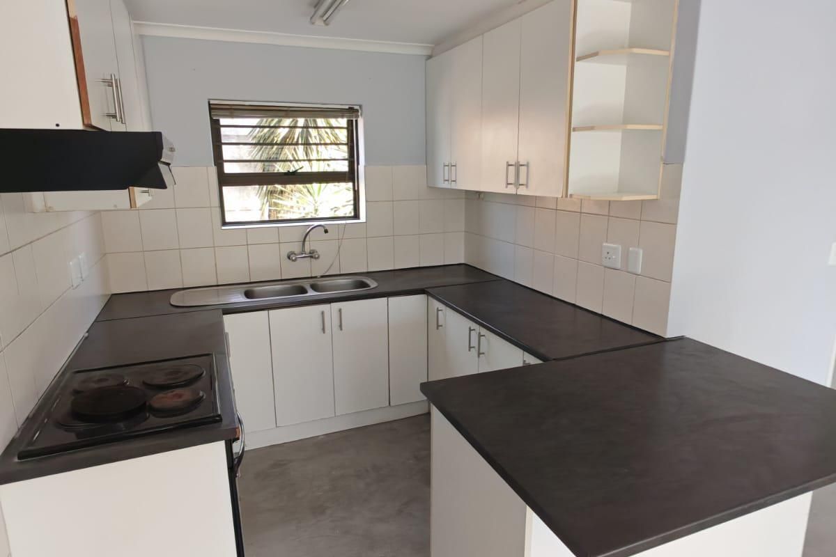 A functional, empty kitchen featuring white cabinetry, dark laminate countertops, a built-in electric hob, and a tiled backsplash.