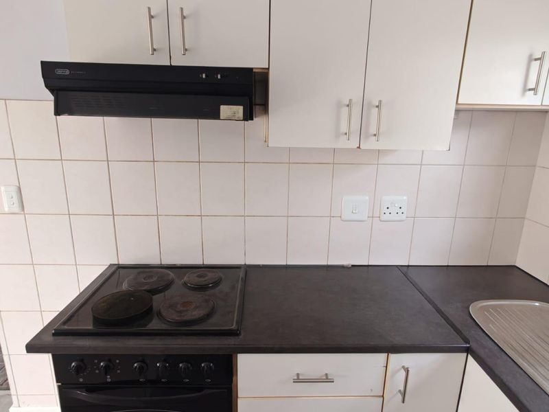 A functional kitchen area featuring white cabinetry, dark laminate countertops, a built-in electric oven and hob, and a tiled backsplash.