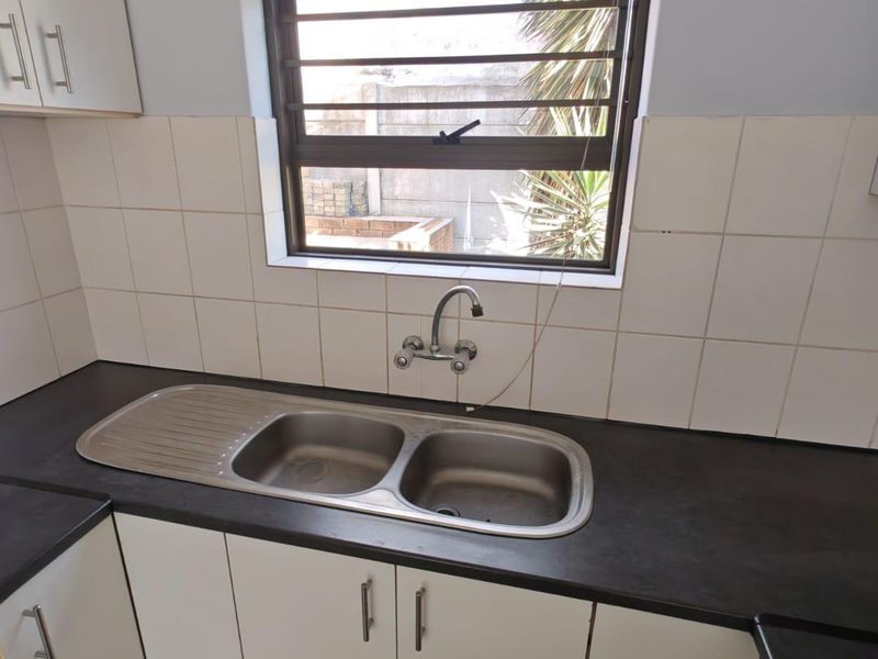 A functional kitchen area featuring a double bowl stainless steel sink, dark laminate countertops, white cabinetry, and a tiled splashback.