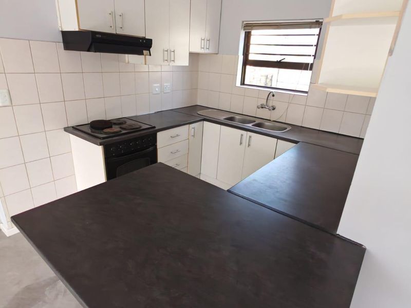 A functional kitchen featuring built-in cabinetry, dark laminate countertops, a stainless steel sink, and an integrated electric stove with an extractor fan.