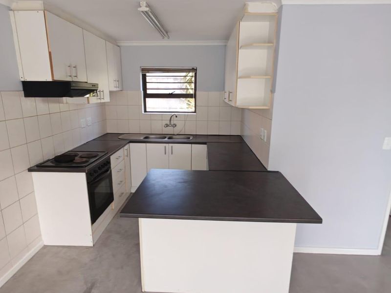 A functional U-shaped kitchen featuring white cabinetry, dark laminate countertops, a built-in stove with extractor, and a tiled splashback.