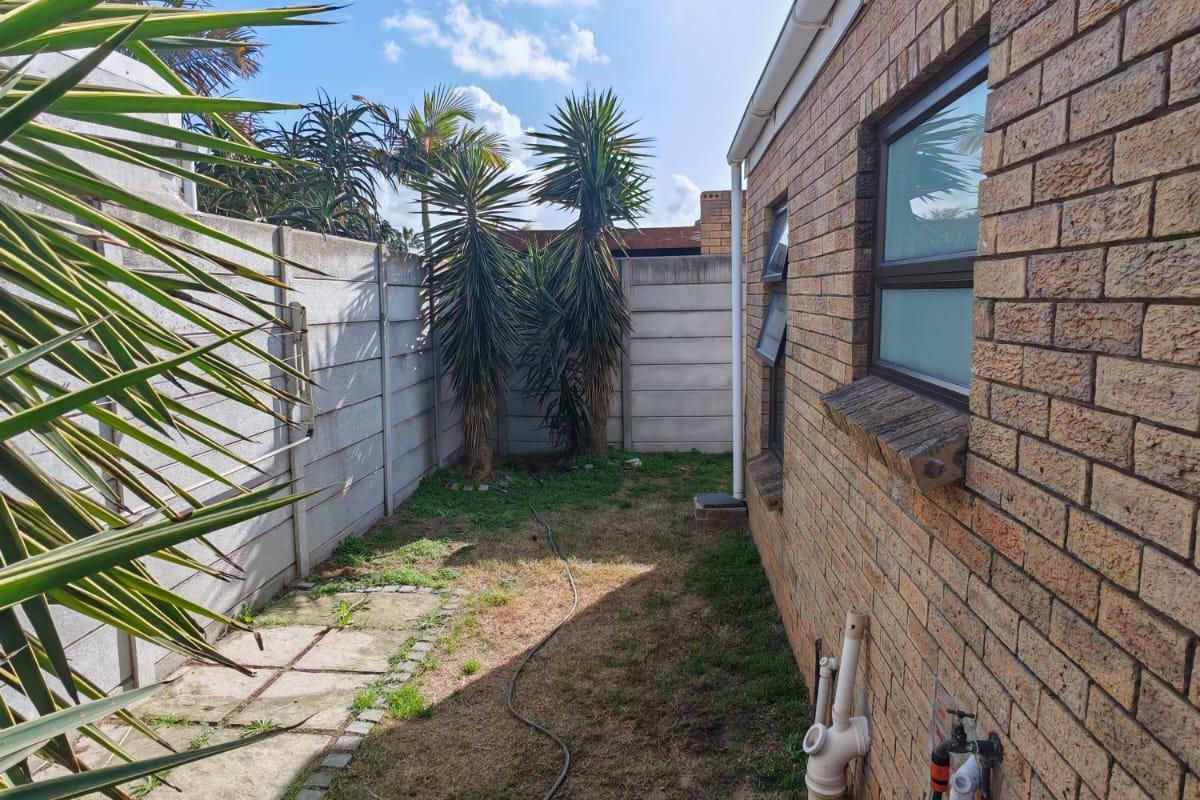 A side exterior view of the property featuring a brick facade, precast boundary wall, and a small garden area with a paved walkway.