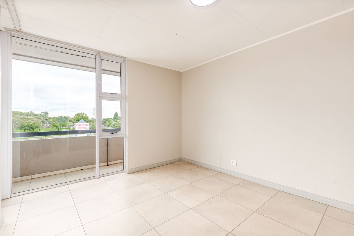 A bright, empty bedroom featuring neutral tiled flooring, a large sliding glass door providing access to a balcony, and clean, minimalist wall finishes.