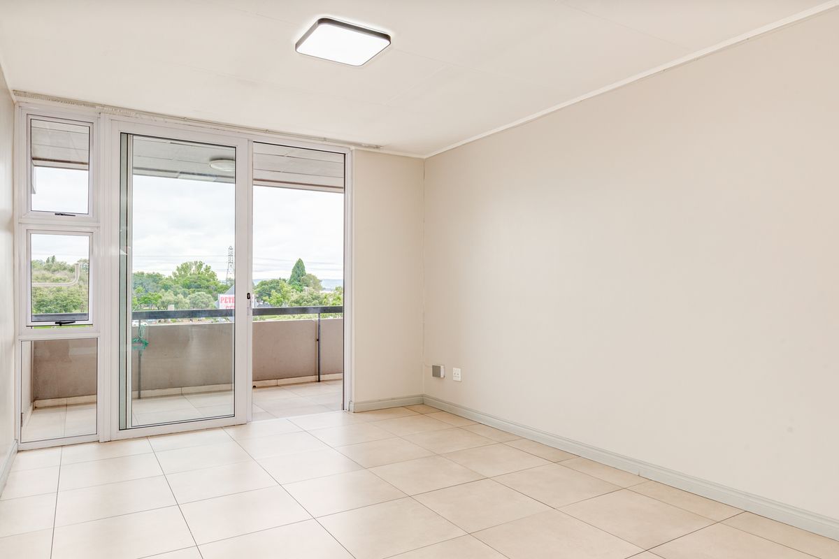 A bright, empty living room featuring neutral floor tiles, a modern ceiling light, and large sliding glass doors leading to an outdoor balcony.