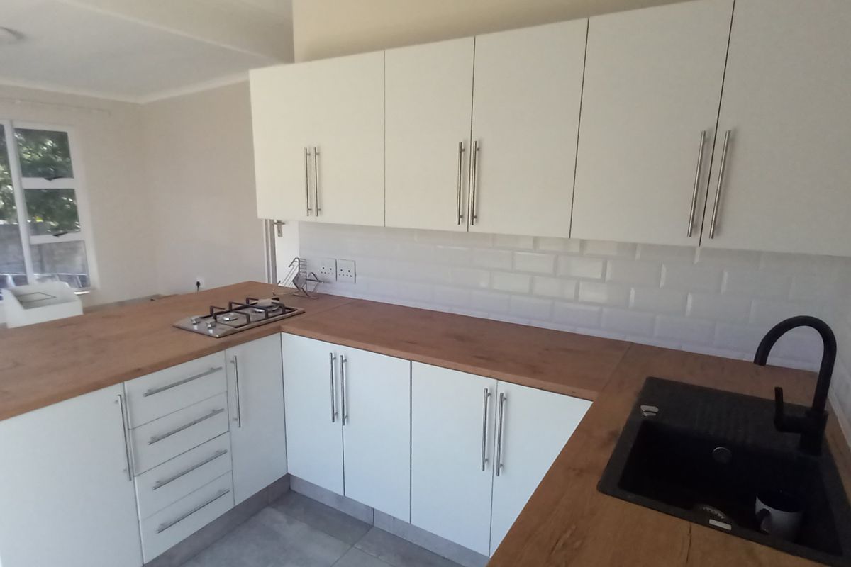 Modern kitchen featuring white cabinetry, wood-look countertops, subway tile backsplash, gas hob, and a black sink with matching tap.