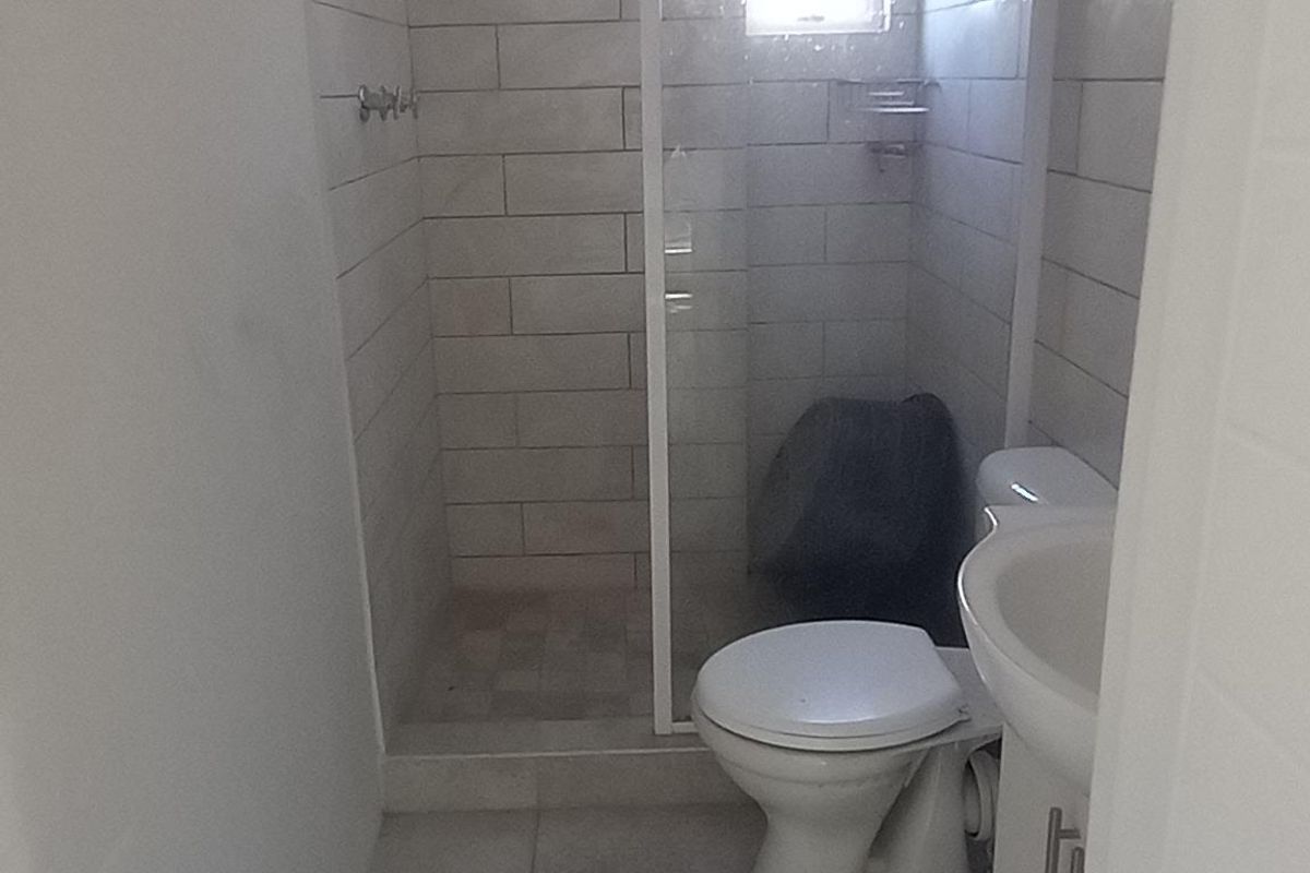 A compact bathroom featuring a shower enclosure, toilet, and pedestal basin with neutral wall and floor tiling.