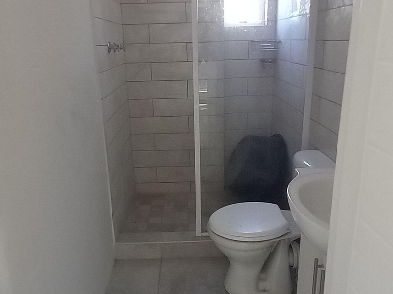 A compact bathroom featuring a shower enclosure, toilet, and pedestal basin with neutral wall and floor tiling.