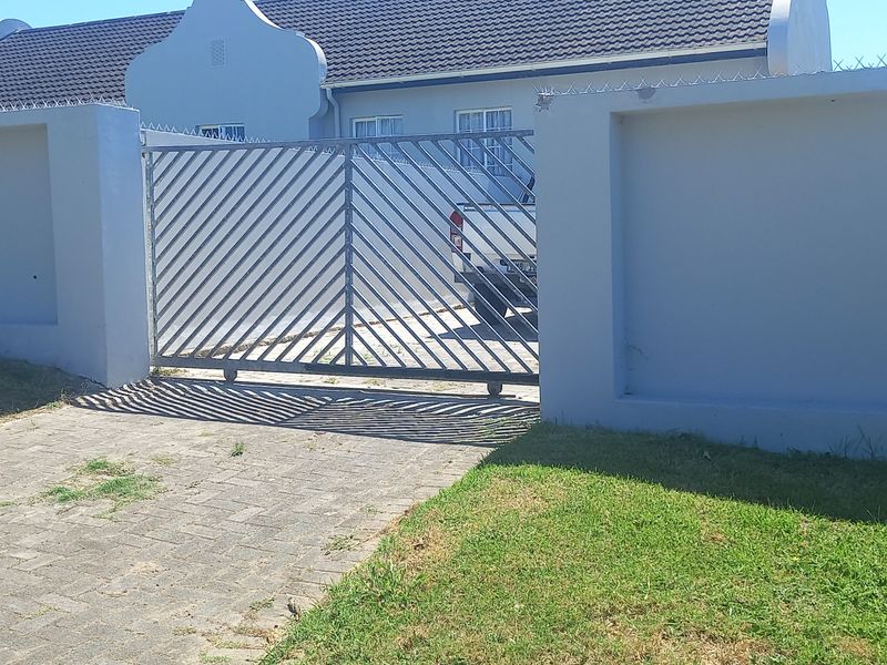 Front view of the property featuring a secure perimeter wall, sliding metal gate, paved driveway, and tiled roof.