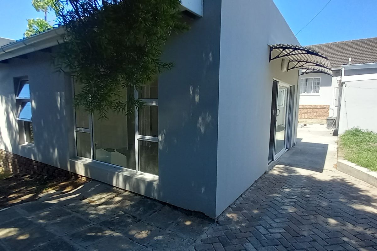 Rear exterior view of the flat featuring a paved patio area, aluminium window frames, and a sliding glass door entrance.