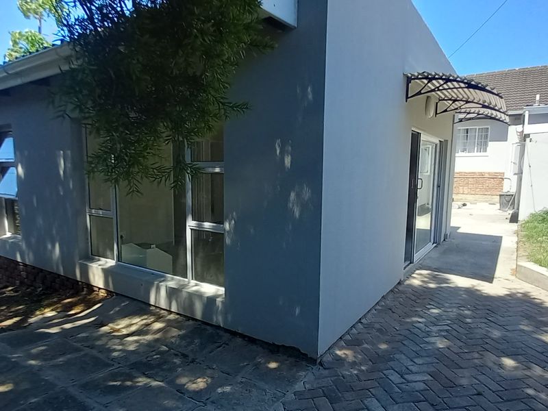 Rear exterior view of the flat featuring a paved patio area, aluminium window frames, and a sliding glass door entrance.
