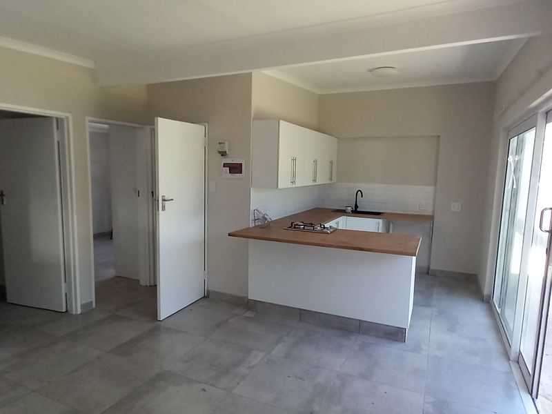 An open-plan living and kitchen area featuring modern white cabinetry, a wooden breakfast bar, gas hob, and large sliding doors leading to the exterior.