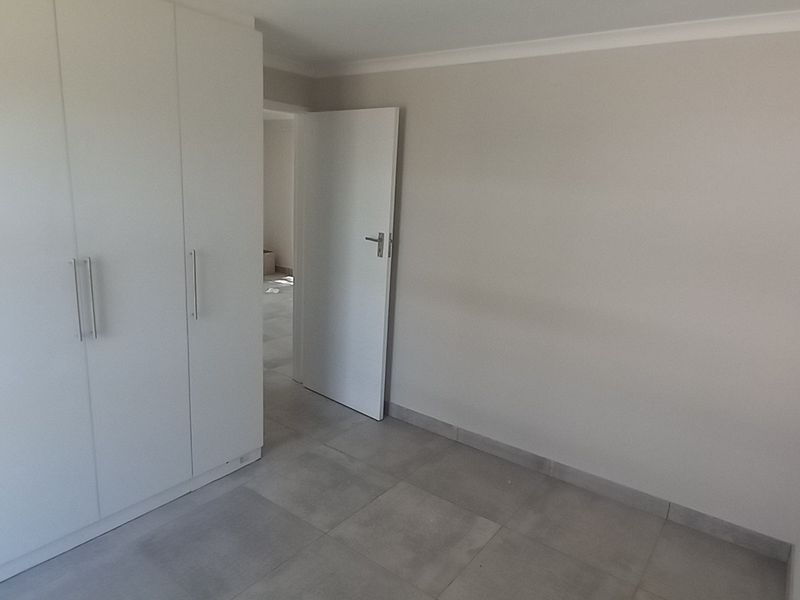 A clean, empty bedroom featuring neutral tiled flooring and modern white built-in cupboards, offering a blank canvas for personalization.