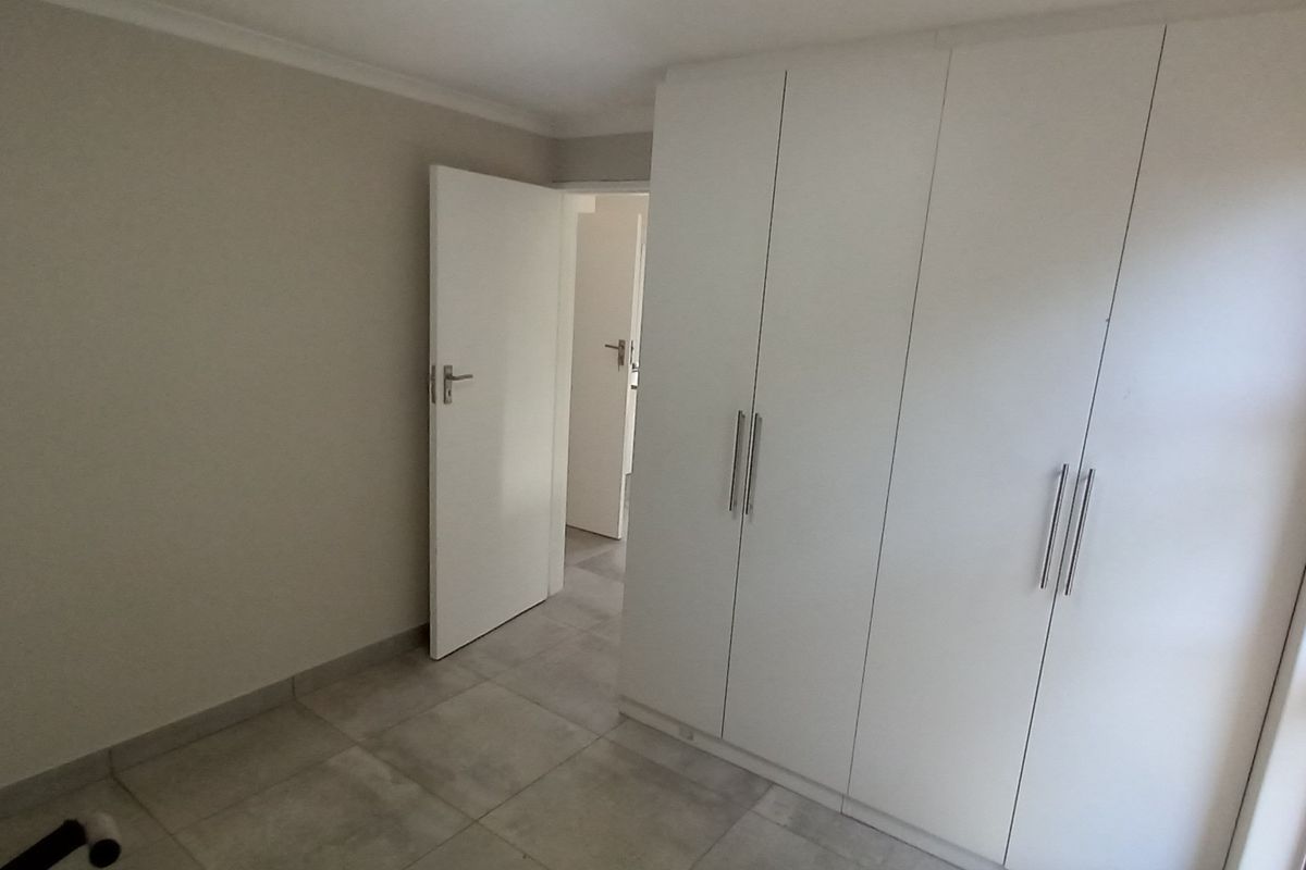 A clean, empty bedroom featuring modern tiled flooring and ample built-in cupboard storage with a neutral color palette.