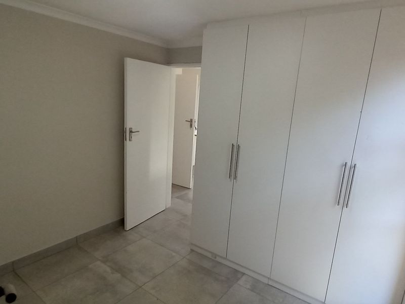 A clean, empty bedroom featuring modern tiled flooring and ample built-in cupboard storage with a neutral color palette.