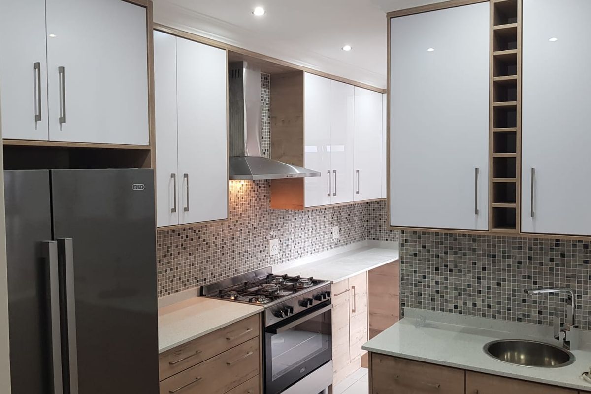Modern kitchen featuring two-tone cabinetry, stone countertops, mosaic tile backsplash, stainless steel gas stove, and integrated extractor fan.