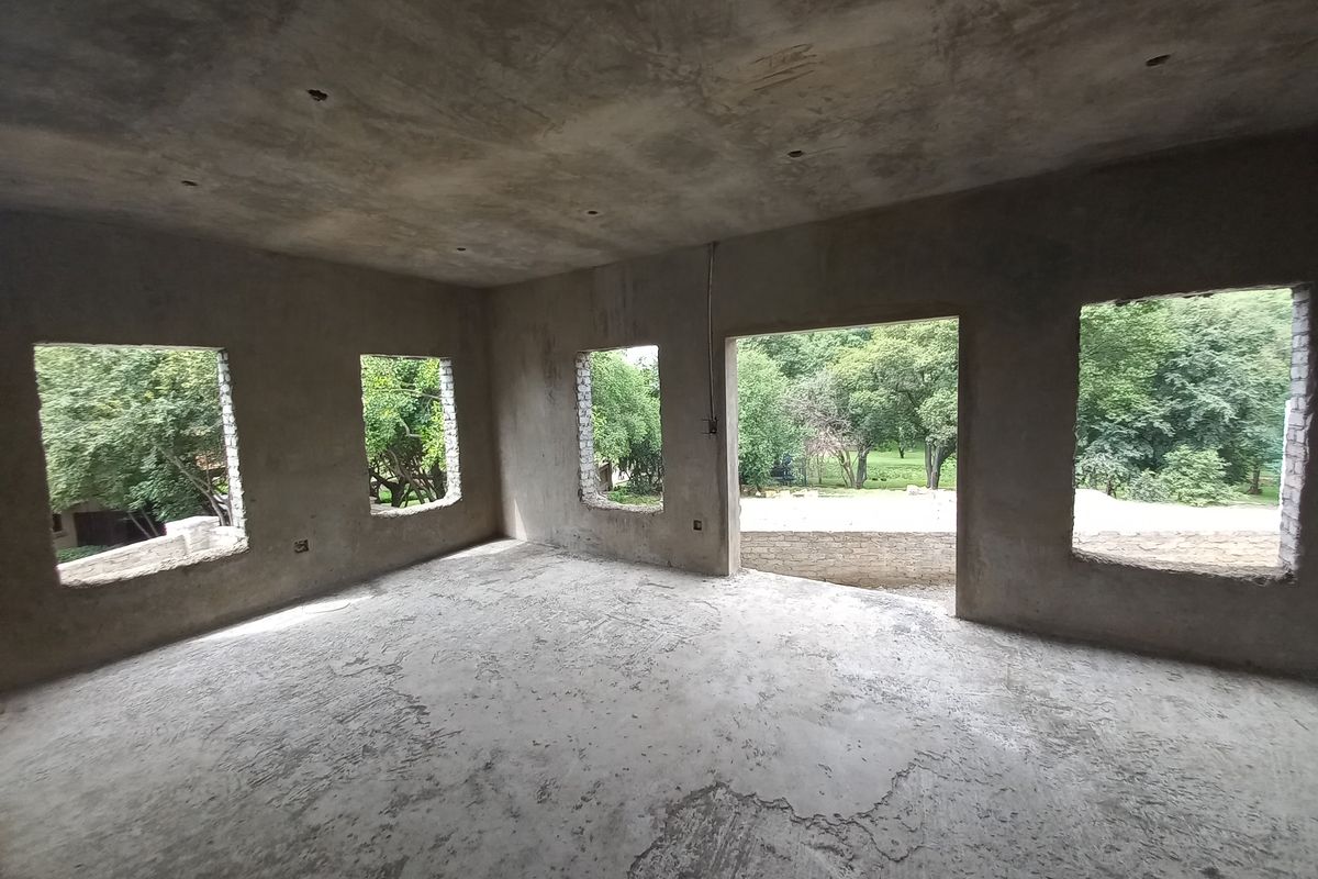 An unfinished interior space in shell condition, featuring raw concrete walls and floors with large openings awaiting window and door installations.