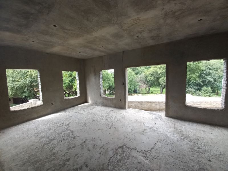 An unfinished interior space in shell condition, featuring raw concrete walls and floors with large openings awaiting window and door installations.
