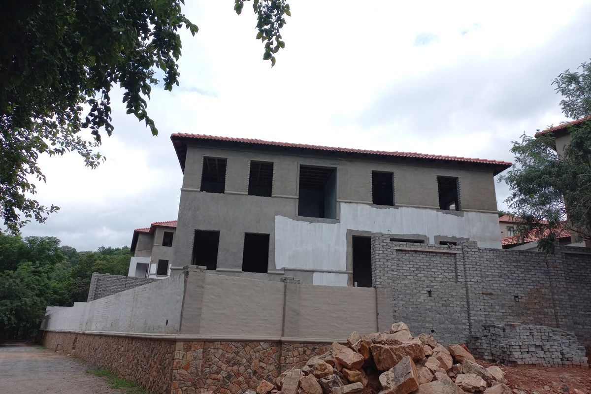 A two-story residential property under construction, featuring a tiled roof, unfinished exterior walls, and stone-clad base, currently in a shell state.