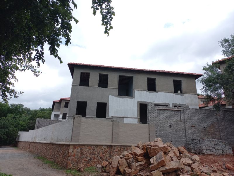 A two-story residential property under construction, featuring a tiled roof, unfinished exterior walls, and stone-clad base, currently in a shell state.