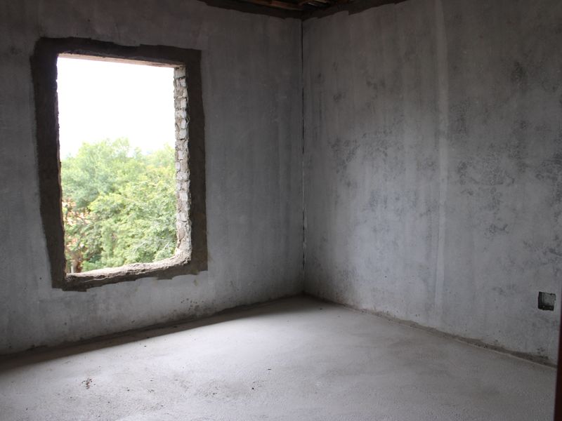 An unfinished bedroom interior featuring raw concrete walls and flooring, awaiting final finishes and window installation.
