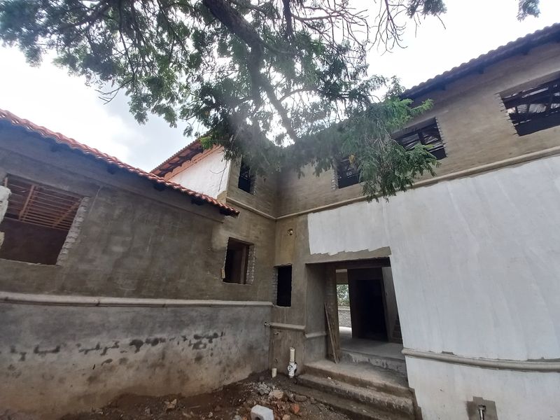Rear view of a house currently under construction, featuring unfinished exterior walls, exposed brickwork, and open window apertures awaiting installation.