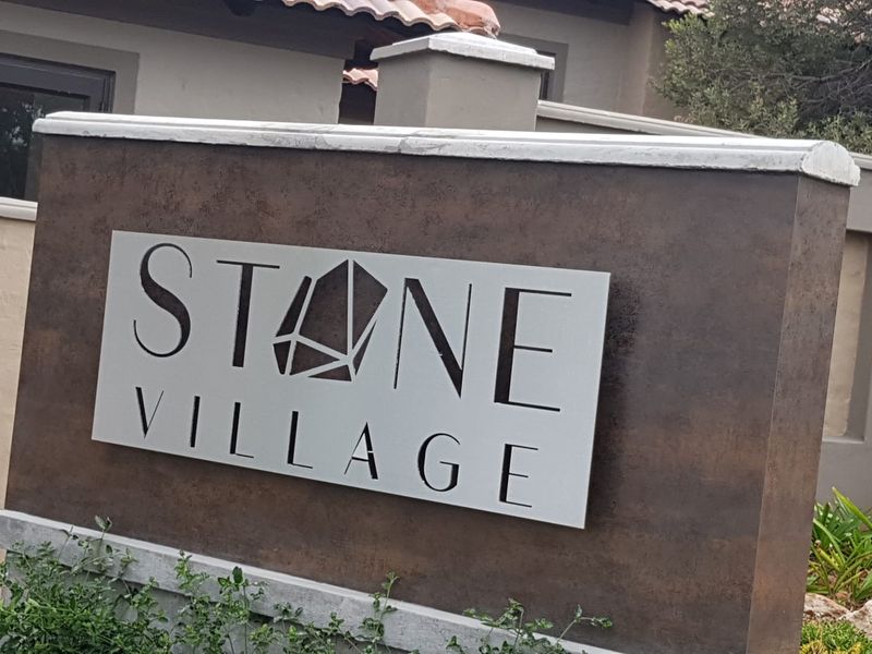 A close-up view of the Stone Village estate signage, featuring a modern metal cut-out design mounted on a textured masonry pillar.