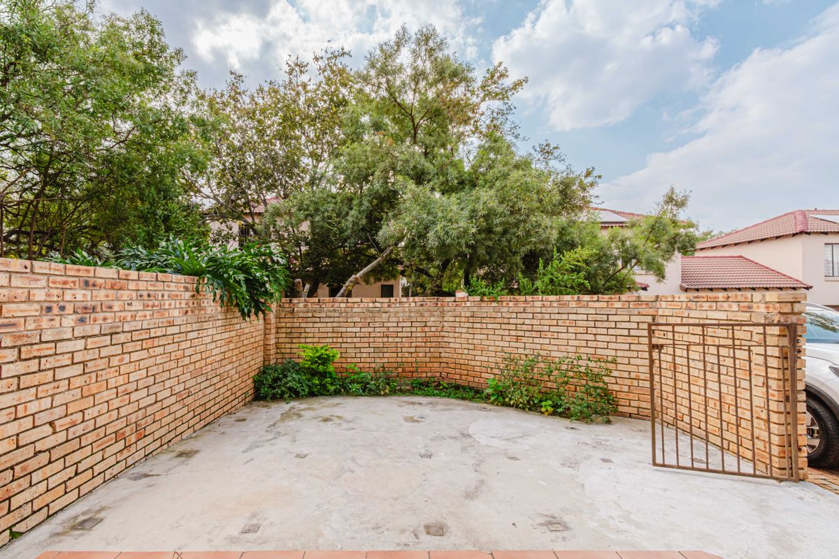 A private outdoor courtyard area featuring high face-brick perimeter walls, concrete flooring, and a metal access gate.