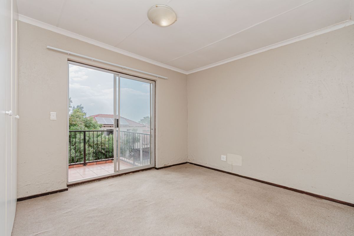 An empty bedroom featuring neutral walls, carpeted flooring, and a sliding glass door providing access to a private balcony.