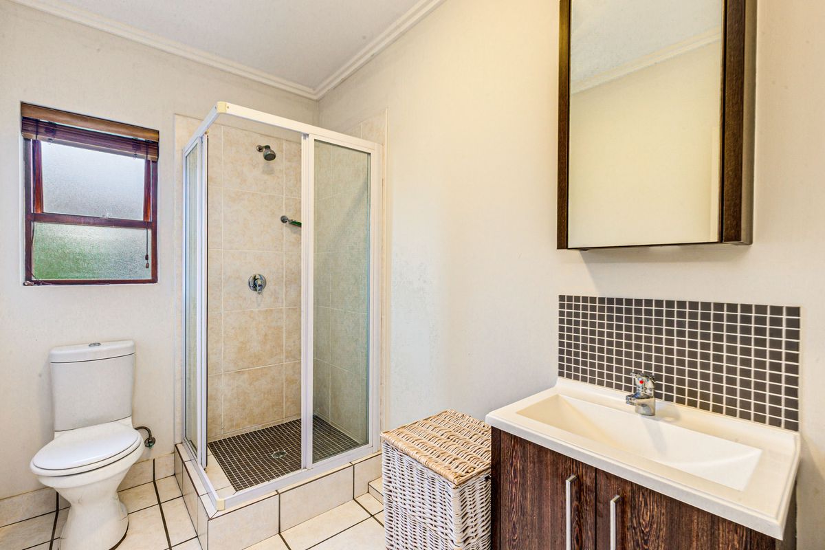 A functional bathroom featuring a glass-enclosed shower, a modern vanity with a tiled splashback, and a standard toilet.