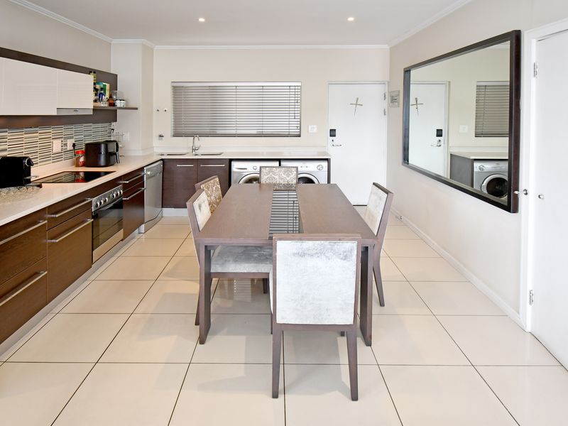 Modern open-plan kitchen and dining area featuring sleek cabinetry, integrated appliances, tiled flooring, and recessed lighting.