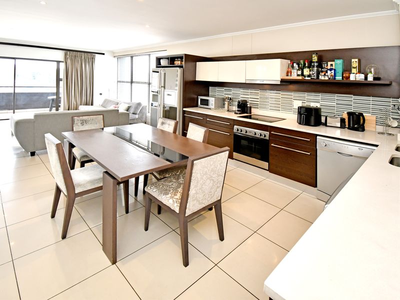 Open-plan living area featuring a modern kitchen with built-in oven, hob, and extractor, flowing into a dining space with access to a balcony.