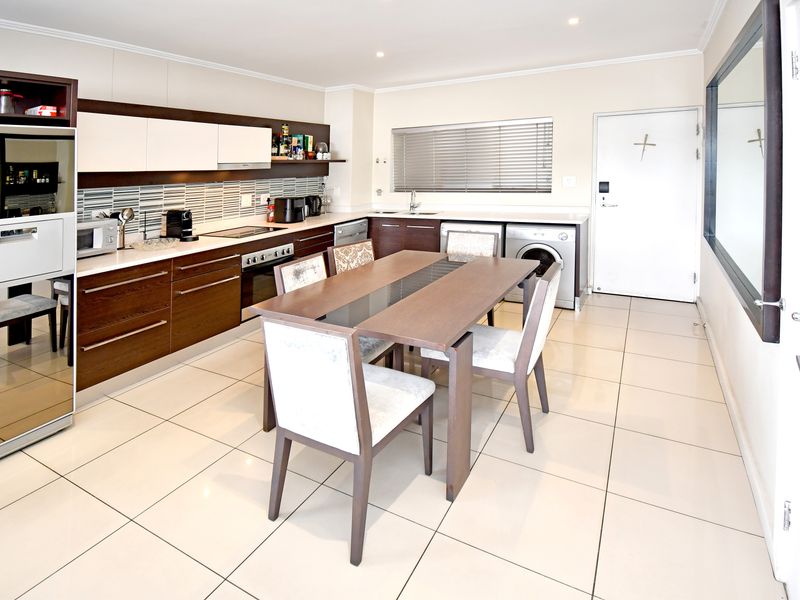 Modern open-plan kitchen and dining area featuring sleek dark wood cabinetry, integrated appliances, tiled flooring, and a clean, contemporary aesthetic.