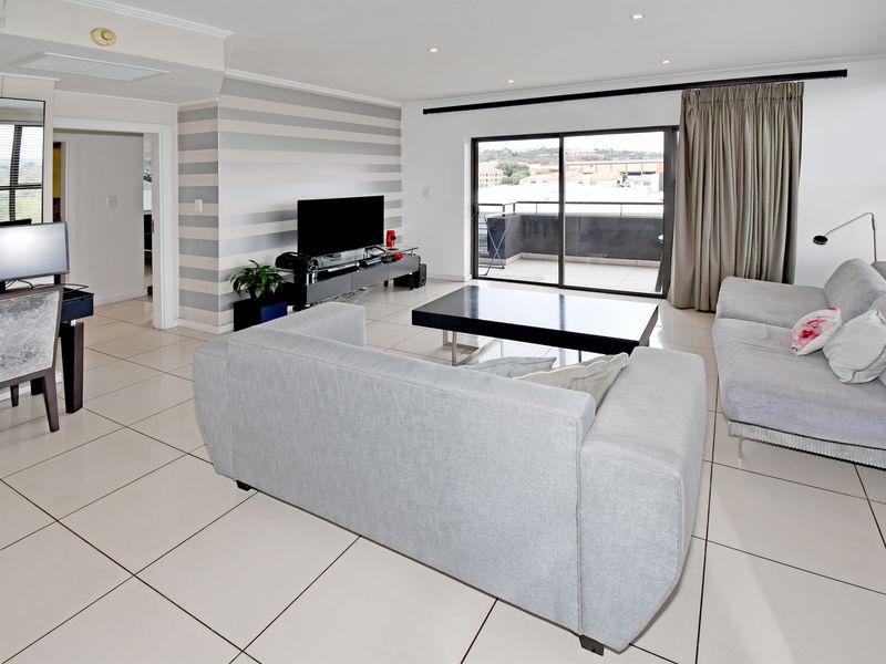 Spacious open-plan living area featuring large format floor tiles, recessed downlighting, and sliding glass doors leading to a private balcony.