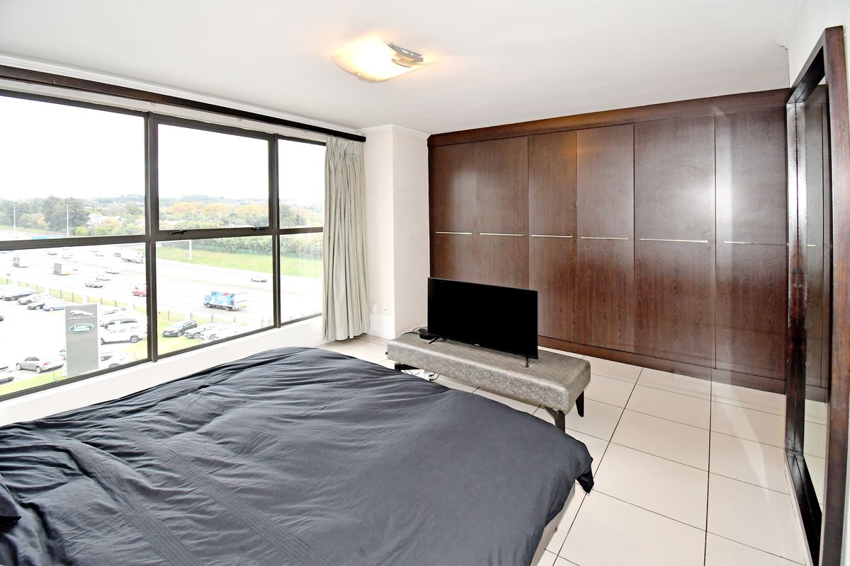 Spacious bedroom featuring large windows with expansive views, tiled flooring, and extensive built-in dark wood cabinetry for ample storage.