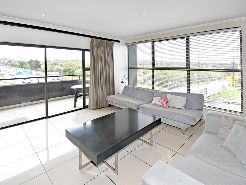 Bright open-plan living area featuring large sliding glass doors leading to a private balcony, tiled flooring, and expansive windows with integrated blinds.