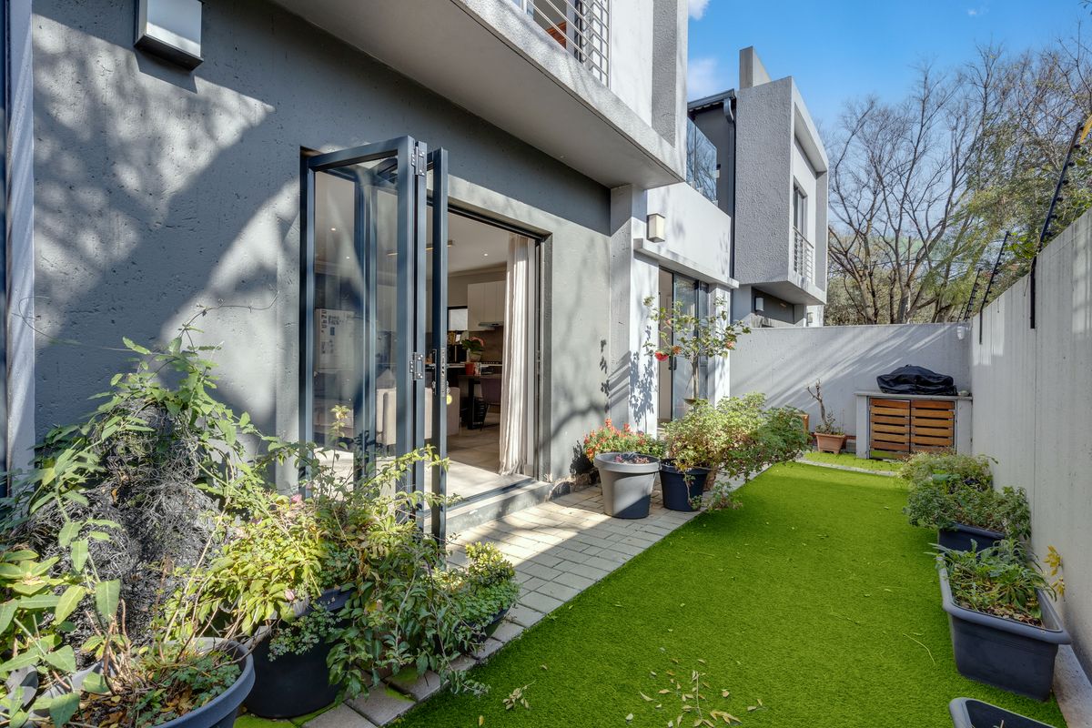 A private rear garden featuring a paved patio area, artificial lawn, and modern folding glass doors providing seamless indoor-outdoor flow.