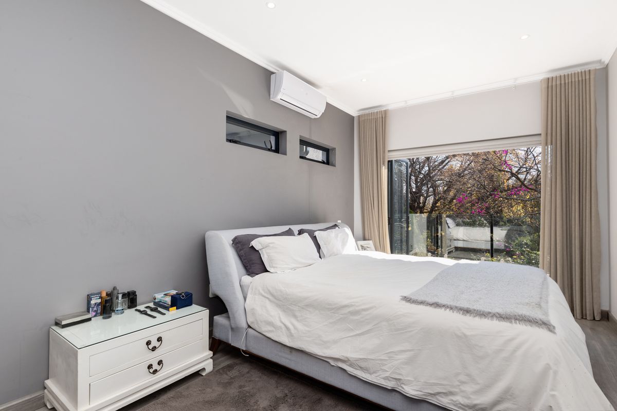 A modern bedroom featuring grey walls, a wall-mounted air conditioning unit, and large glass sliding doors that open to a private garden view.