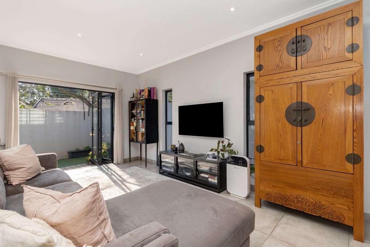 A bright living room featuring tiled flooring, recessed ceiling lighting, and large black-framed folding doors that open directly onto a private rear patio area.