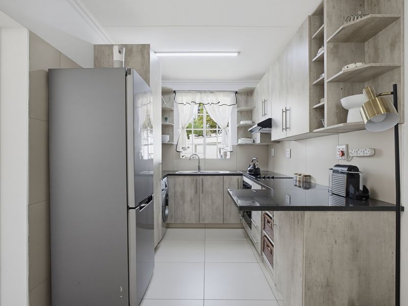 Modern galley-style kitchen featuring light wood-grain cabinetry, sleek black granite countertops, integrated sink, and tiled flooring with efficient layout.