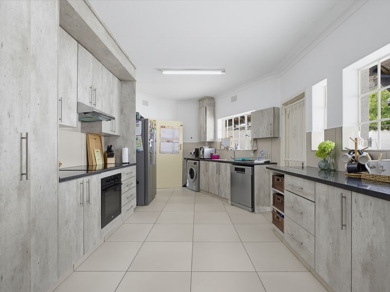 A functional galley-style kitchen featuring light wood-look cabinetry, dark countertops, integrated oven, hob, extractor fan, and dedicated space for laundry appliances.