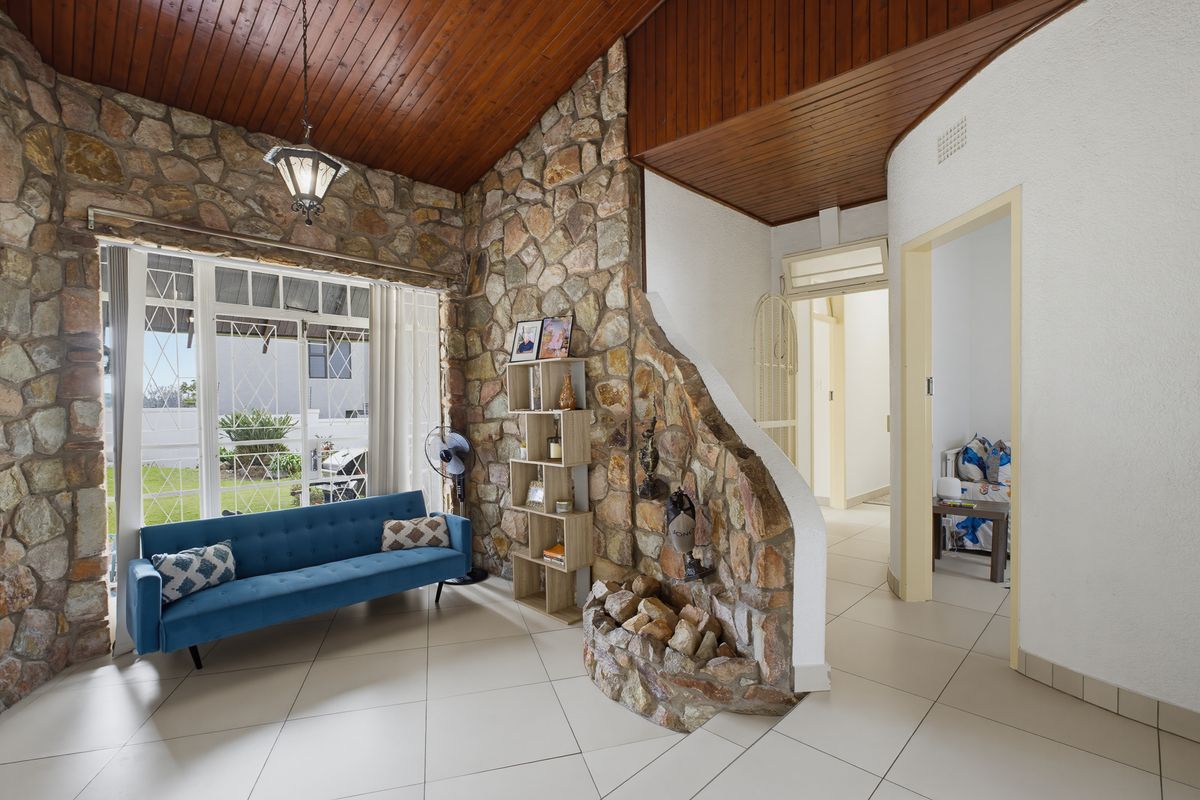 Living area featuring a distinctive natural stone feature wall, vaulted timber ceiling, and large windows providing natural light and garden views.