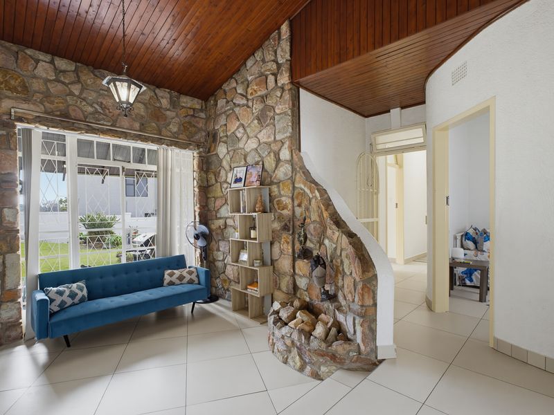 Living area featuring a distinctive natural stone feature wall, vaulted timber ceiling, and large windows providing natural light and garden views.