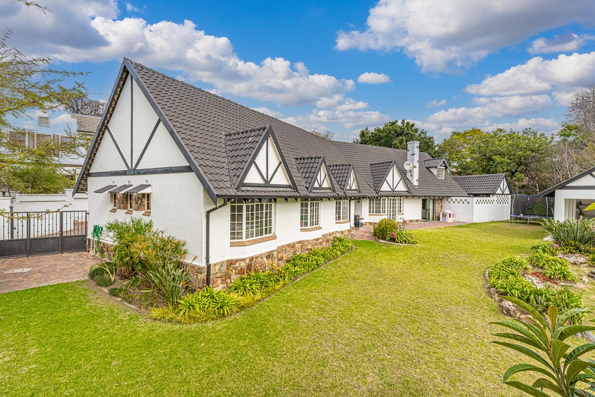 A well-maintained Tudor-style house featuring a dark tiled roof, stone base detailing, and a spacious landscaped garden with a paved patio area.